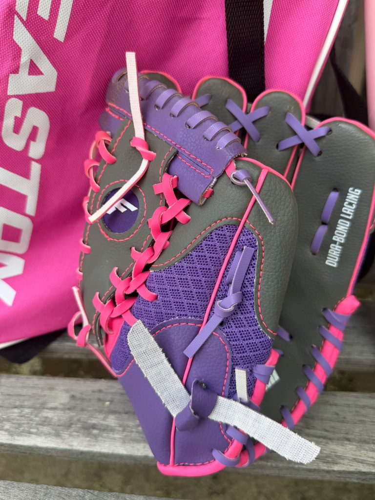 Purple and pink youth softball glove beside T-ball bag