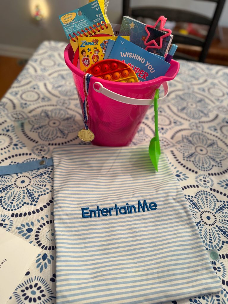 Pink graduation bucket behind a blue striped Entertain Me pouch for organizing small summer activities.