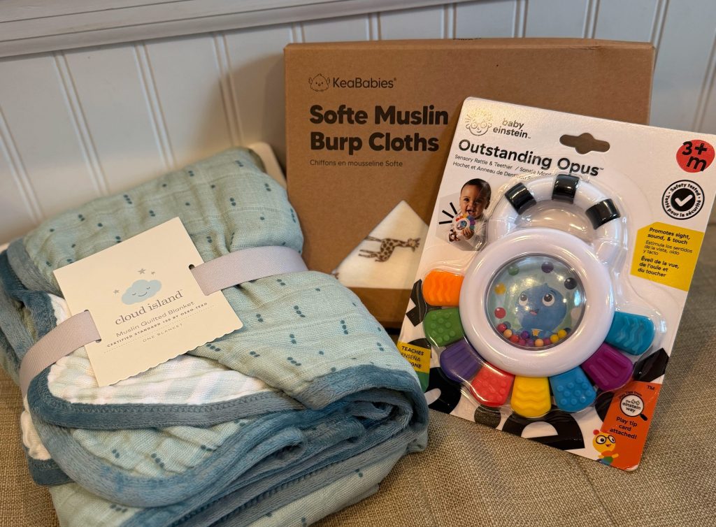 Baby gift extras and toddler toys sorted from a birthday gift bin, including a muslin blanket, burp cloths, baby sensory toy, and toddler toys.