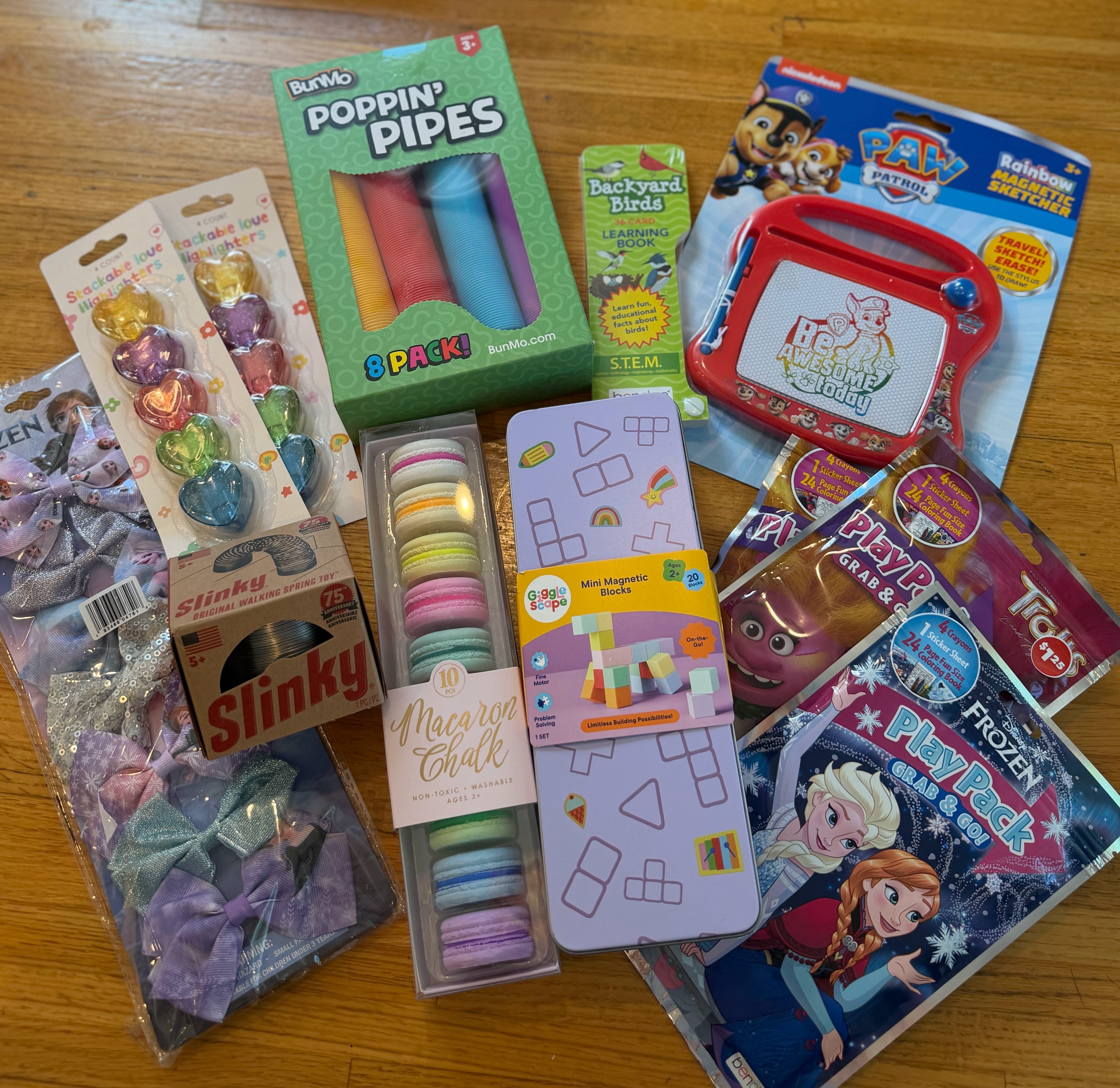 Small kids’ activity items including Play Packs, chalk, stickers, bows, slinky, mini magnetic blocks, highlighters, and small toys sorted from a birthday bin.