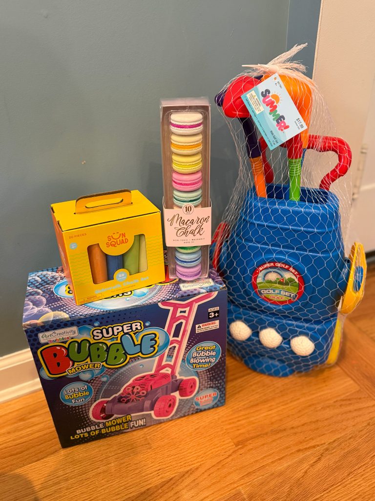 Outdoor birthday gift ideas including sidewalk chalk, macaroon chalk, a bubble mower, and a kids’ golf set arranged on the floor.
