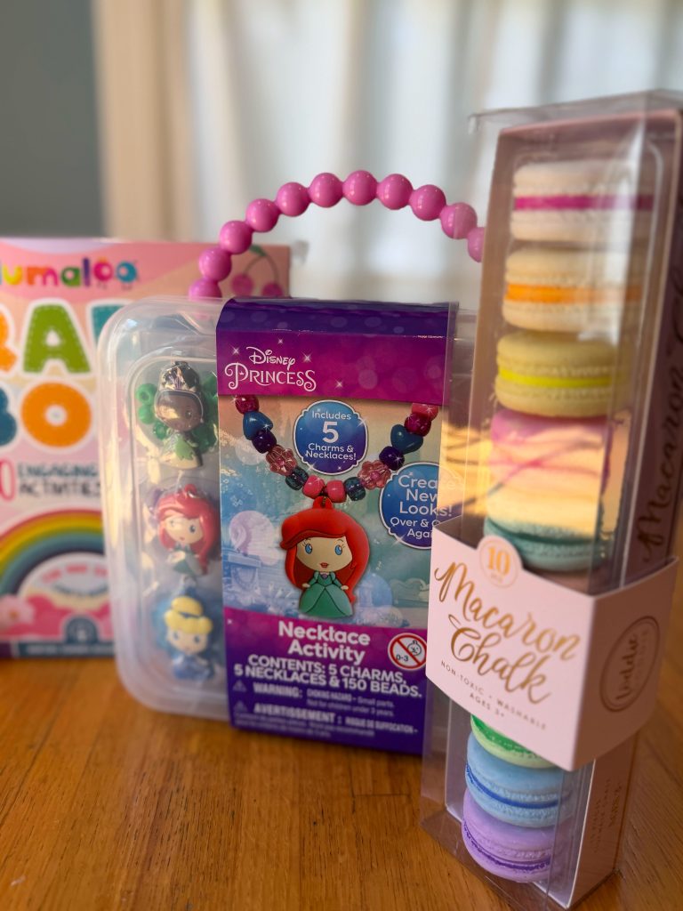 Complete craft-themed birthday gift for a 4-year-old arranged on a wooden table with a craft box, necklace kit, small character toys, highlighters, and chalk.