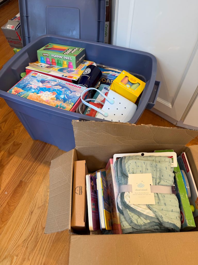 Two storage bins filled with organized kids’ birthday gifts, activity books, craft kits, baby gifts, and small toys after a birthday bin reset.